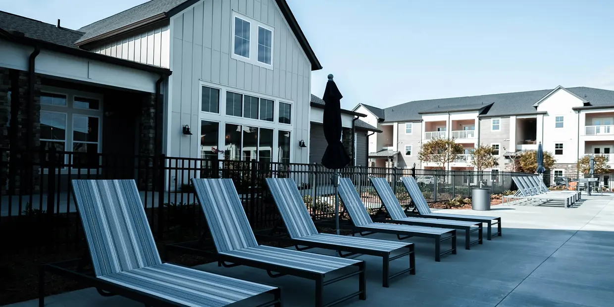 Lounge chairs on a patio beside a clubhouse and garden-style apartment buildings